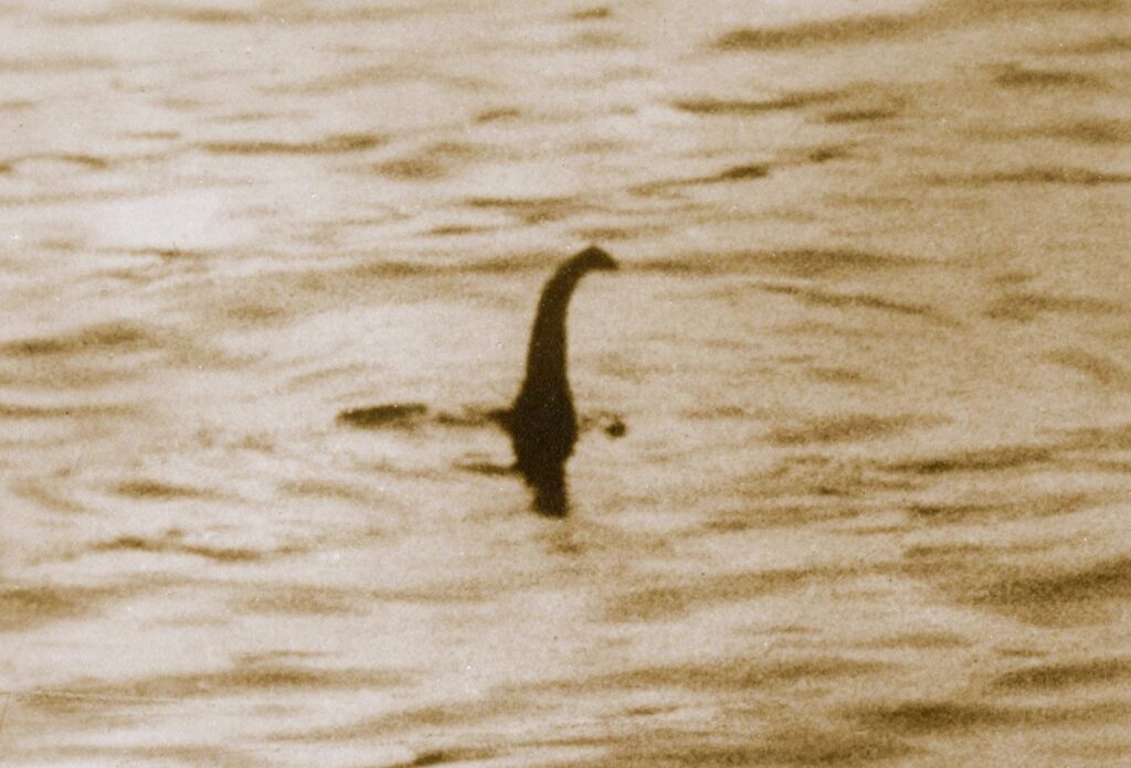 Sepia-toned photo of a long-necked figure emerging from rippling water, widely known as the classic Loch Ness Monster image.