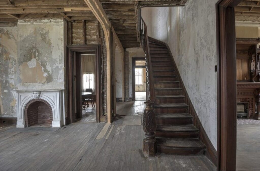 Old house interior with worn wooden staircase and peeling walls, showing signs of age rather than haunting